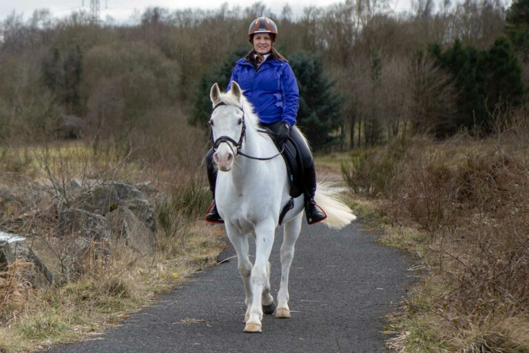 Woman riding white horse down pathway