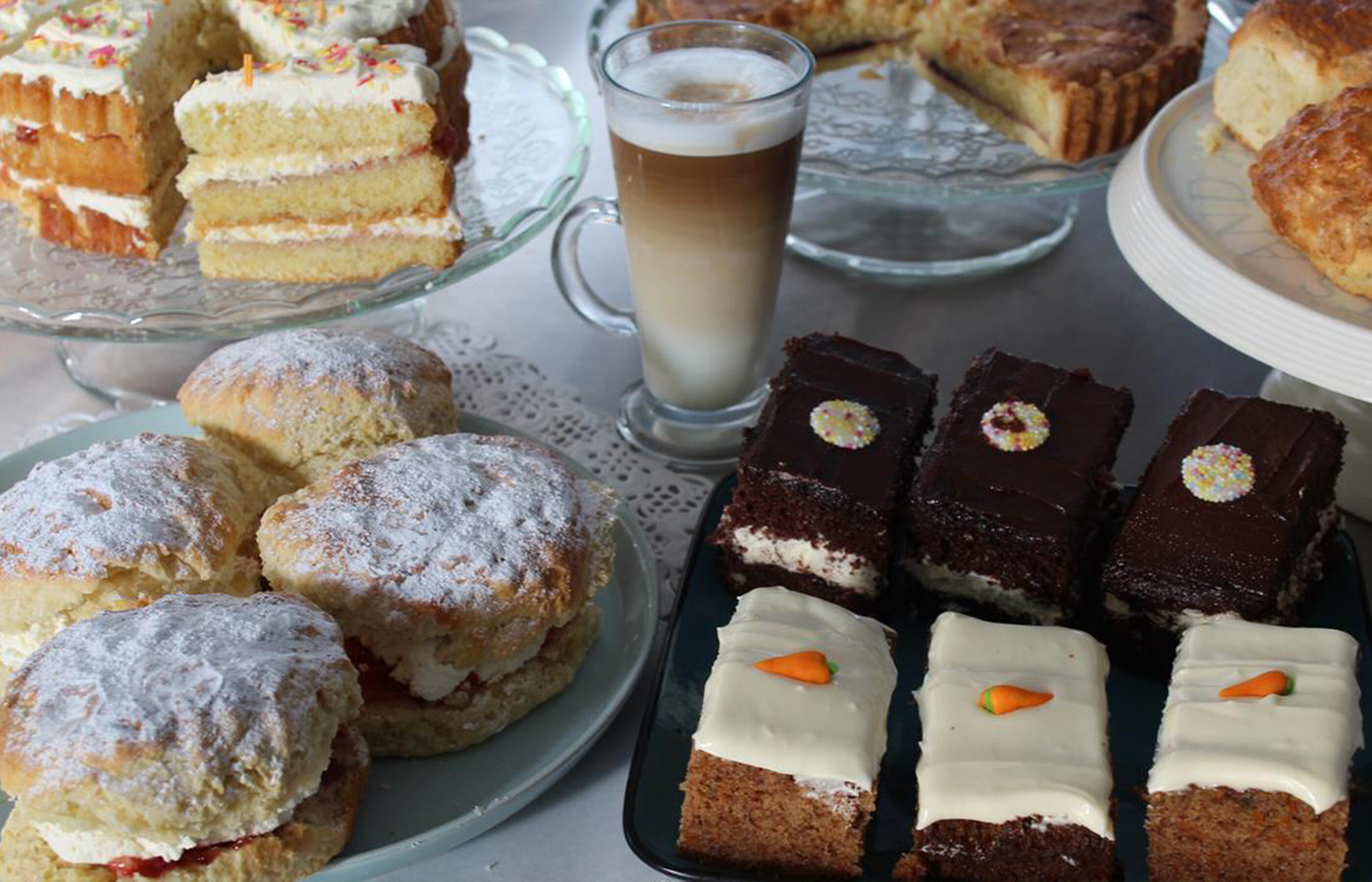 Close-up of a selection of plates of cakes, scones and a section of a tart with a glass of iced coffee in the centre.